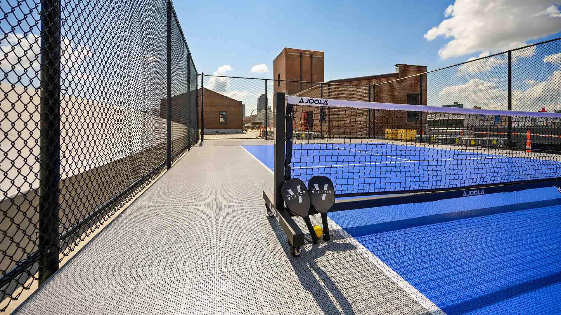 Rooftop pickleball court with large metal fence.
